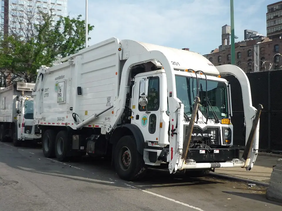 A white New York City Department of Sanitation collection truck parked at the curb.